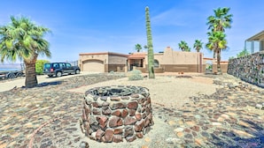 A courtyard with a stone fire pit, palm trees, and a building with a red-tiled roof. - Patio & Panoramic Views: Hillside Lake Havasu Home (Lake Havasu City)