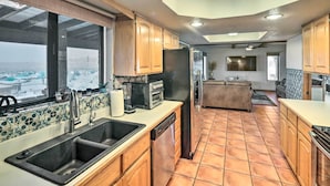 A kitchen with wooden cabinets, a black dishwasher, and a large window overlooking a cityscape. - Patio & Panoramic Views: Hillside Lake Havasu Home (Lake Havasu City)