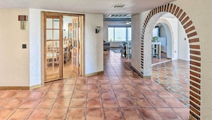 A spacious hallway with tiled flooring, a wooden door leading to a dining area, and an arched brick wall. - Patio & Panoramic Views: Hillside Lake Havasu Home (Lake Havasu City)