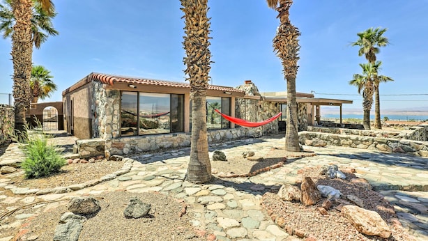 A stone building with a tiled roof, surrounded by palm trees and a hammock. - Patio & Panoramic Views: Hillside Lake Havasu Home (Lake Havasu City)