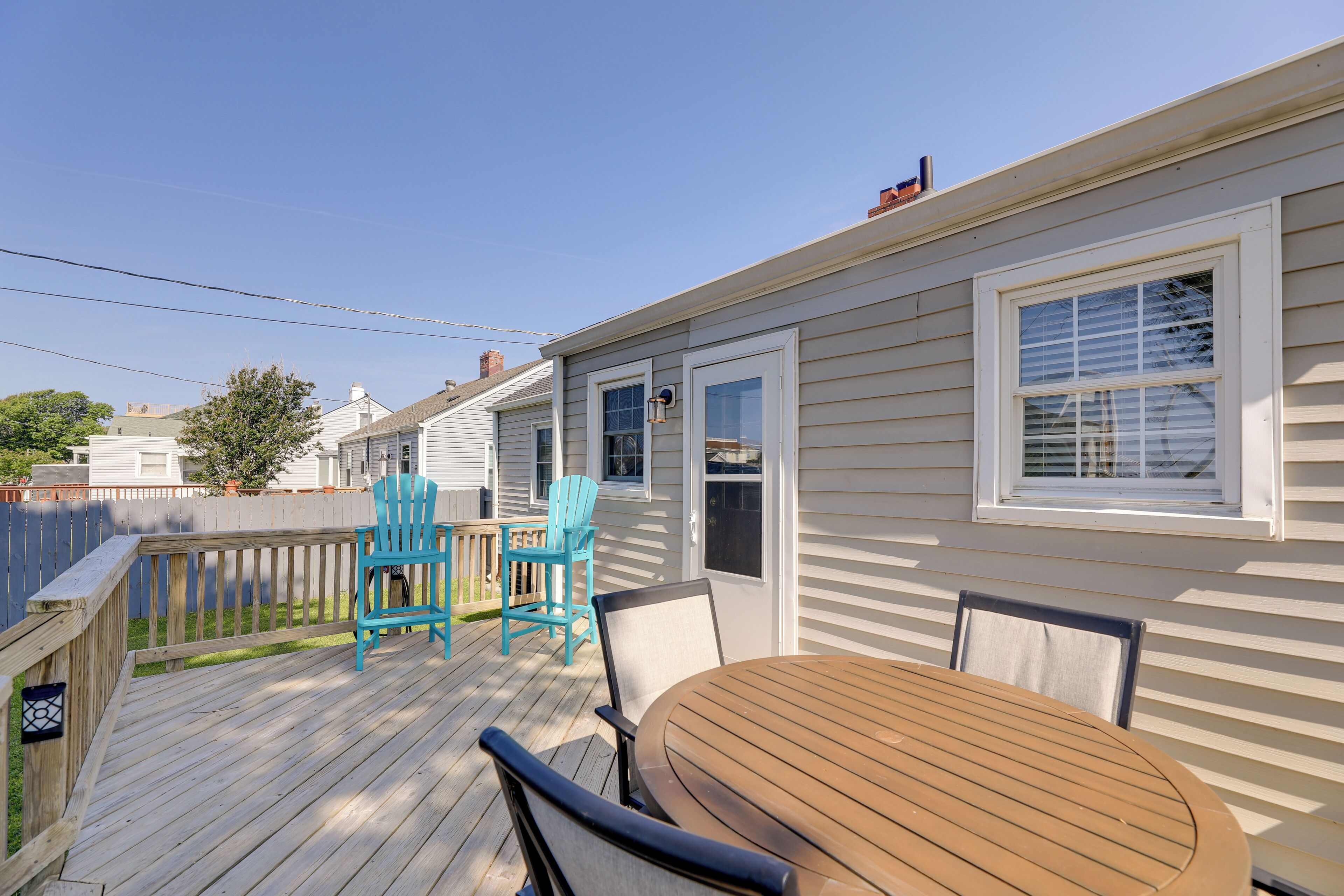 A wooden deck with a round table and four chairs, a wooden fence, and a house with white siding and a chimney.