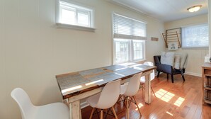 A dining area with a wooden table, white chairs, and a chair with cushions. There are windows with blinds and a ladder leaning against the wall. - North Carolina Retreat - Deck, Grill & Creek Views (Beaufort)