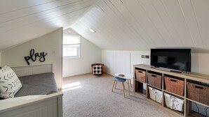 A cozy attic bedroom with a bed, a TV, and storage baskets. - North Carolina Retreat - Deck, Grill & Creek Views (Beaufort)