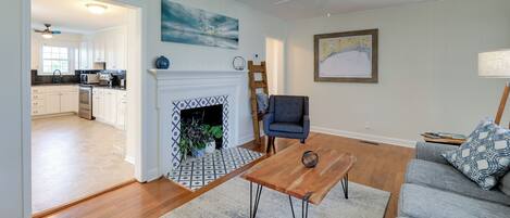 A living room with a fireplace, a sofa, a coffee table, and a view into the kitchen.
