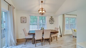Ein Esszimmer mit Holztisch und Stühlen, einer Kristalllüster und großen Fenstern mit Jalousien.