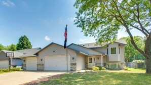 A two-story house with a garage, a basketball hoop, and a flagpole with an American flag. - Sporty Blaine Home w/ Games ~ 2 Mi to Super Rink! (Blaine)