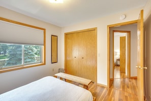 Une chambre à coucher comprenant un lit, un banc en bois, une armoire et une porte donnant sur une autre pièce.