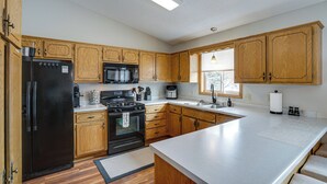 A kitchen with wooden cabinets, a black refrigerator, a stove, and a large island with a countertop. - Sporty Blaine Home w/ Games ~ 2 Mi to Super Rink! (Blaine)