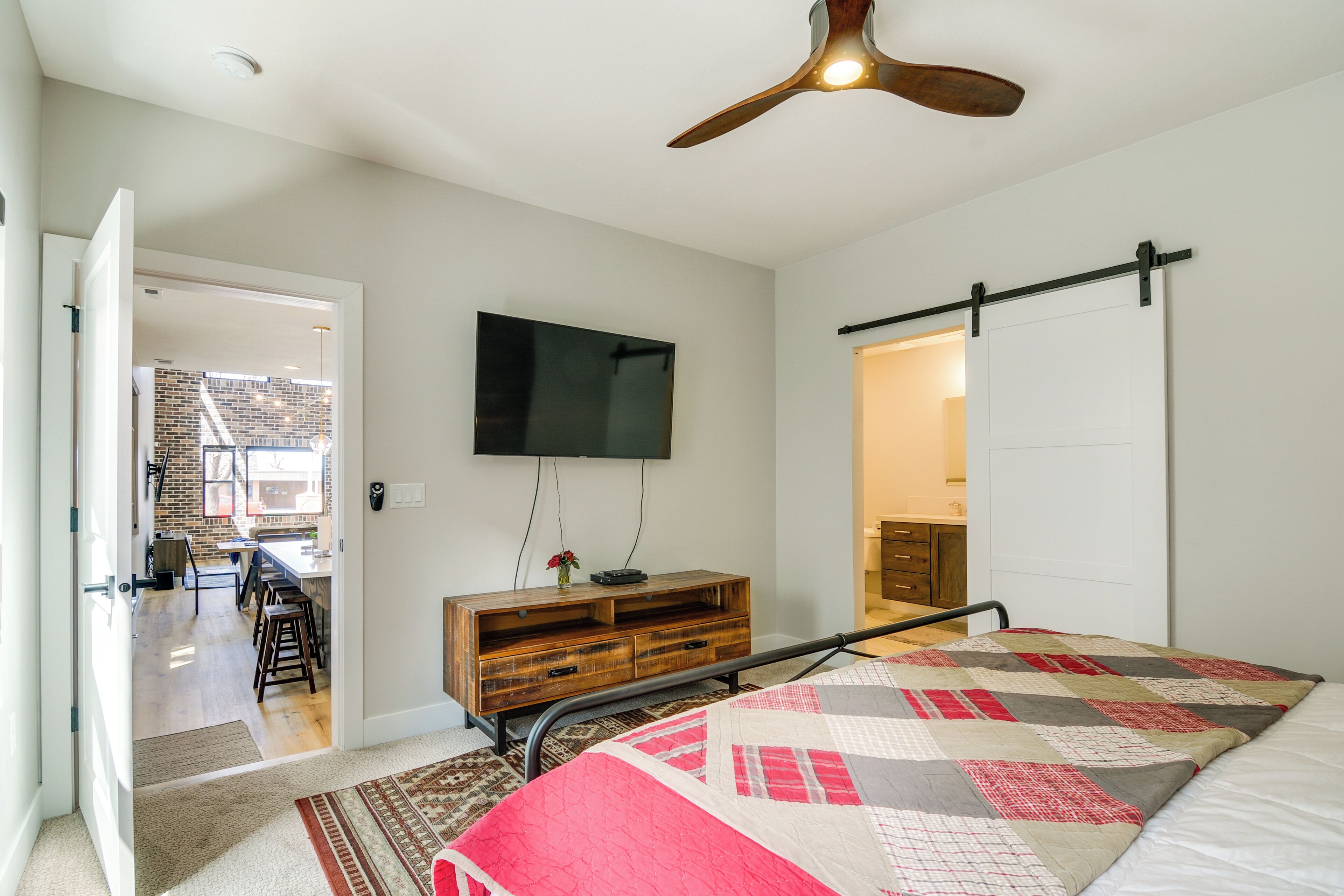 A bedroom with a bed, a wooden dresser, a flat-screen TV, and a ceiling fan.