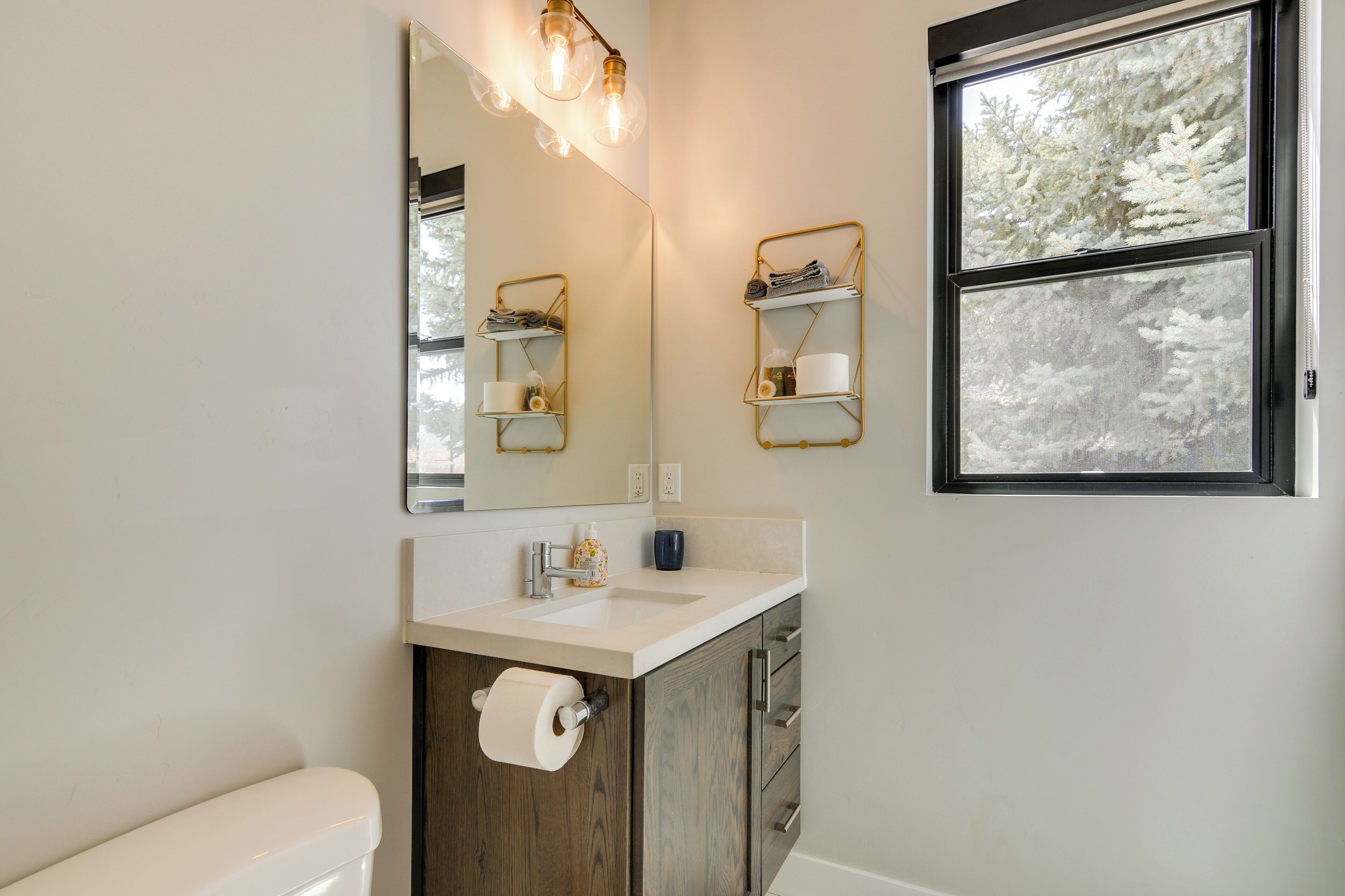 Une salle de bain avec un lavabo blanc, un meuble en bois et un miroir doté d’étagères.