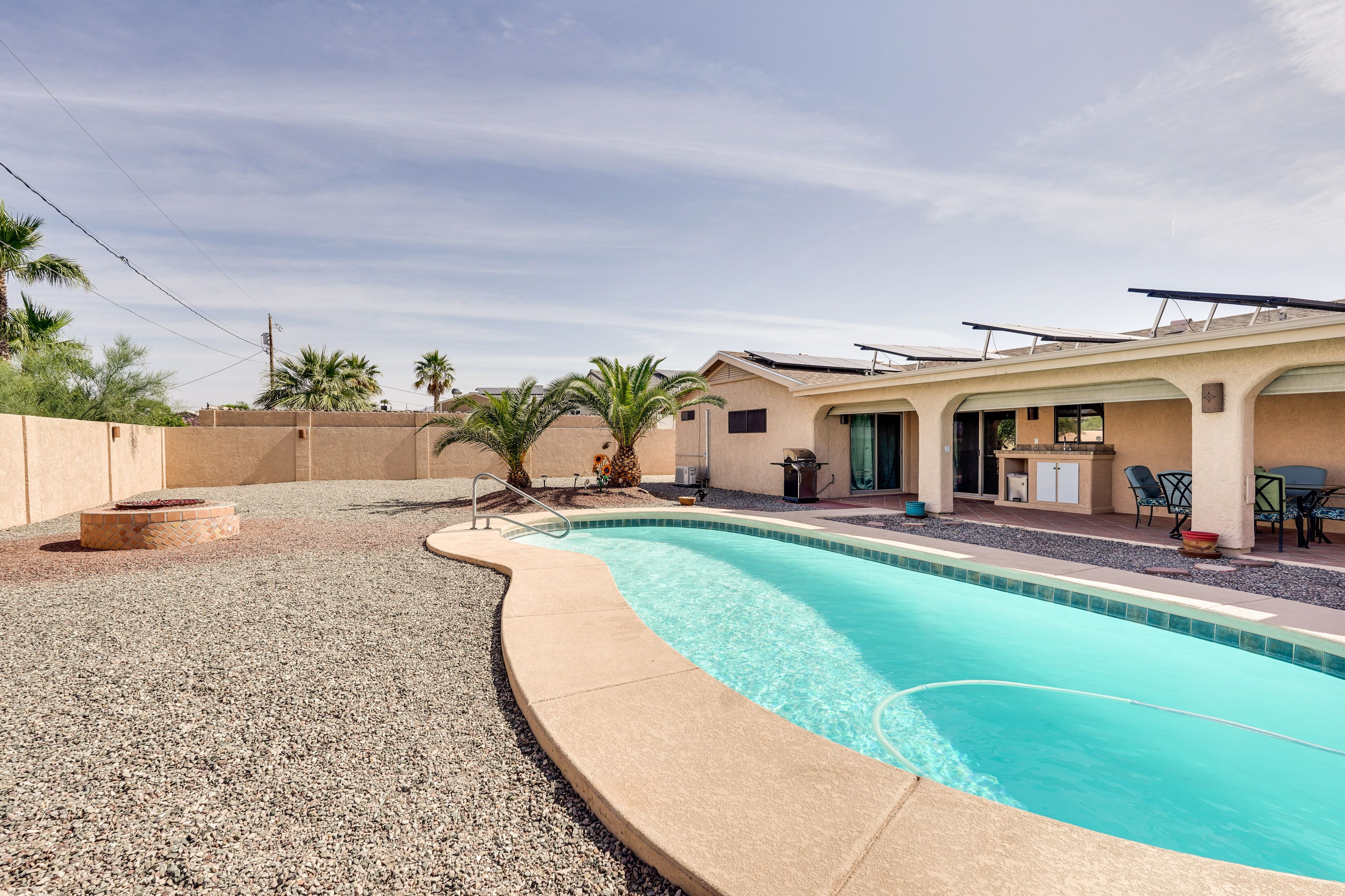 A swimming pool with a curved edge, a patio area with chairs and a table, and a building with a flat roof.