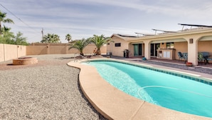 Ein Pool mit gewölbter Kante, eine Terrassenfläche mit Stühlen und Tisch sowie ein Gebäude mit flachem Dach.