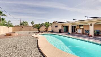 A swimming pool with a curved edge, a patio area with chairs and a table, and a building with a flat roof.