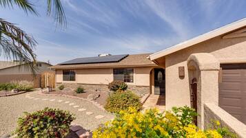 A residential house with a solar panel, a driveway, and a garden with yellow flowers.