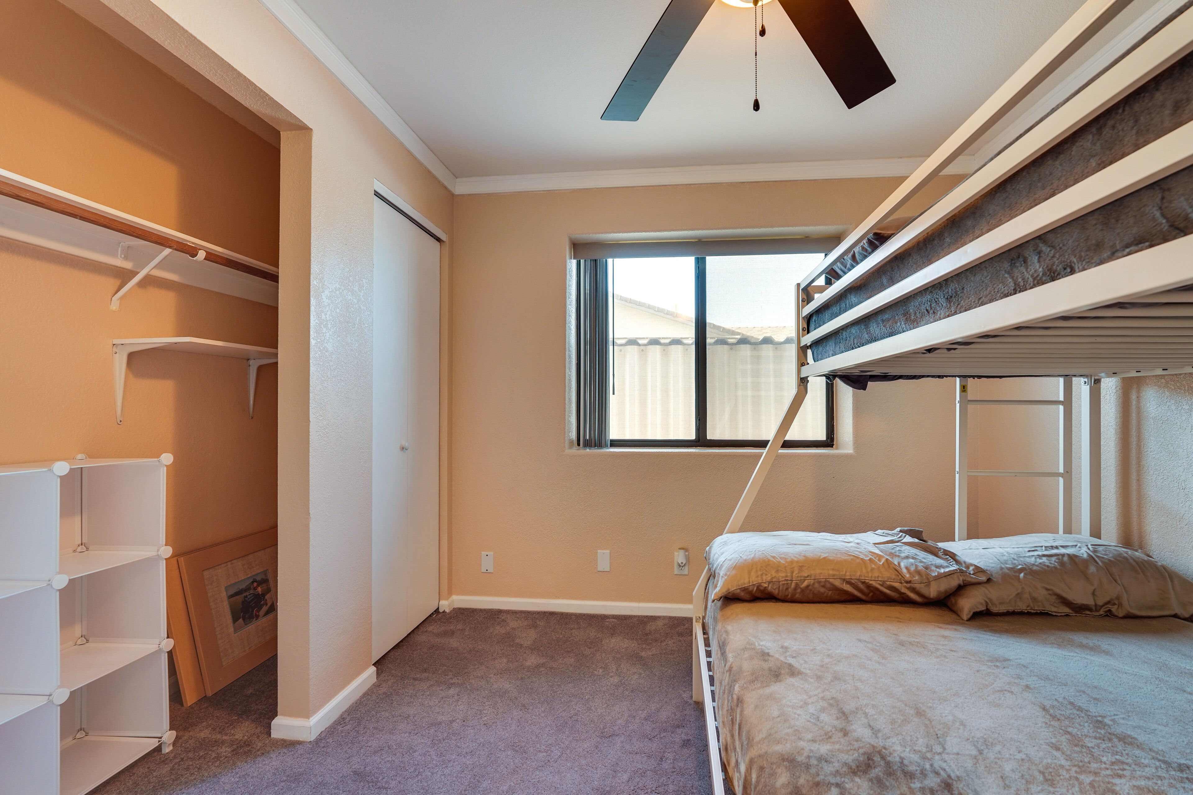 Une chambre avec des lits superposés, un placard avec des étagères et une fenêtre avec des stores.