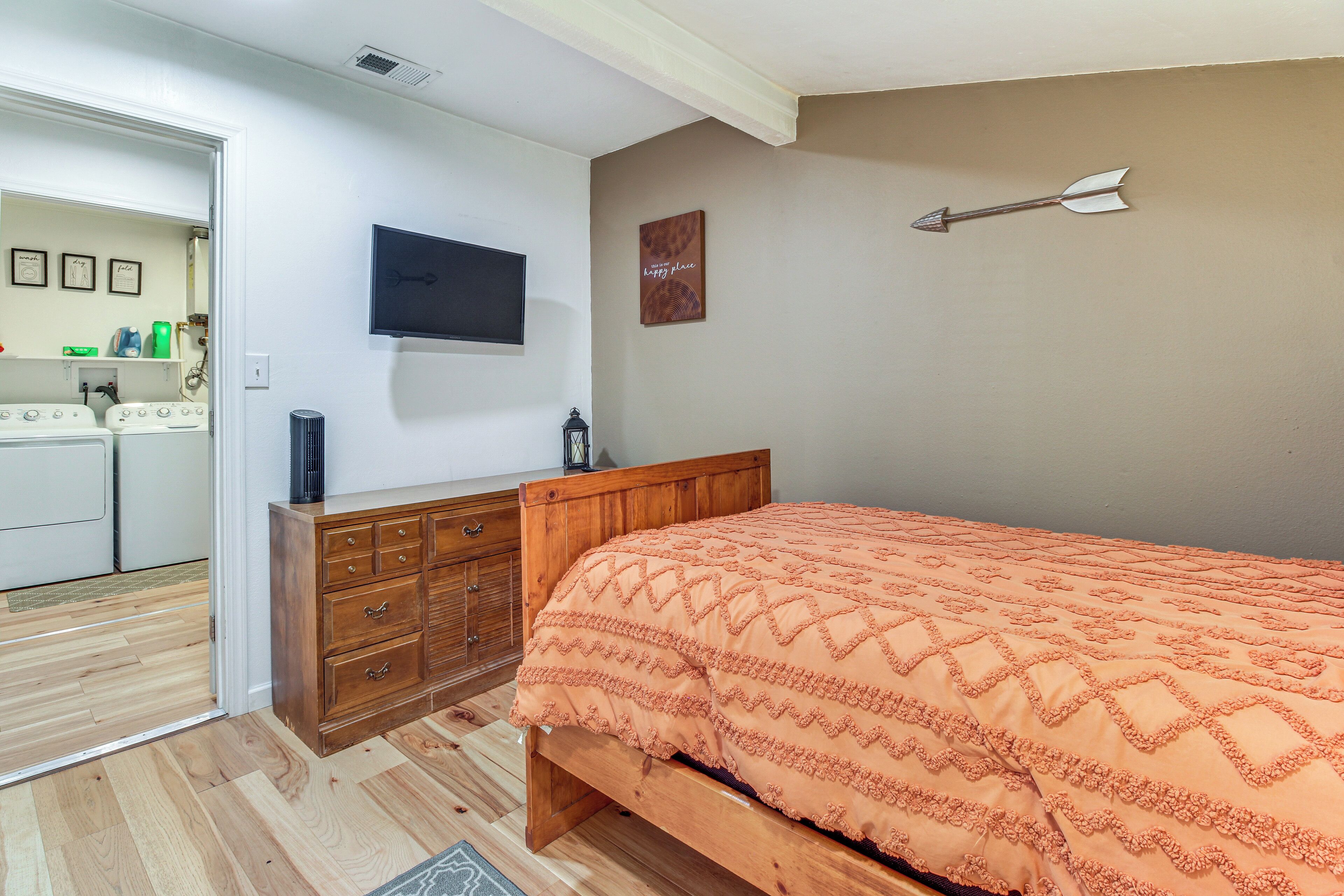 A bedroom with a wooden bed, a television mounted on the wall, and a small cabinet.