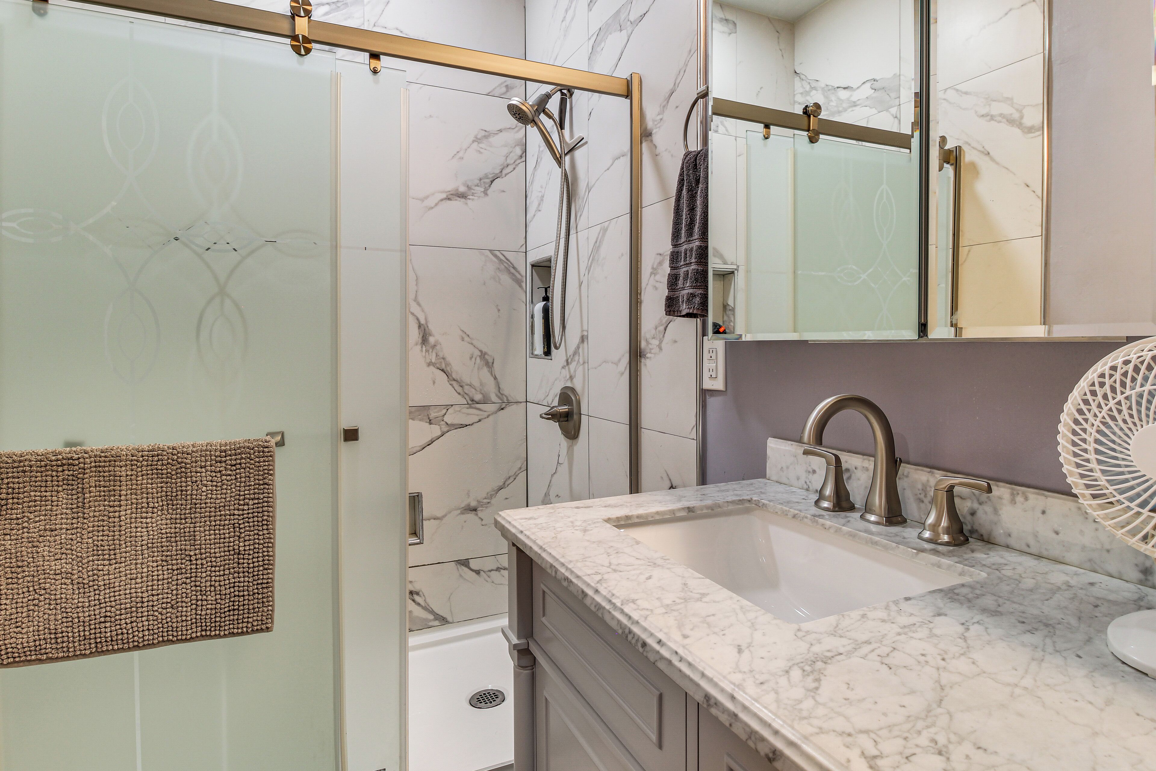 A bathroom with a glass shower door, a sink with a marble countertop, and a large mirror.