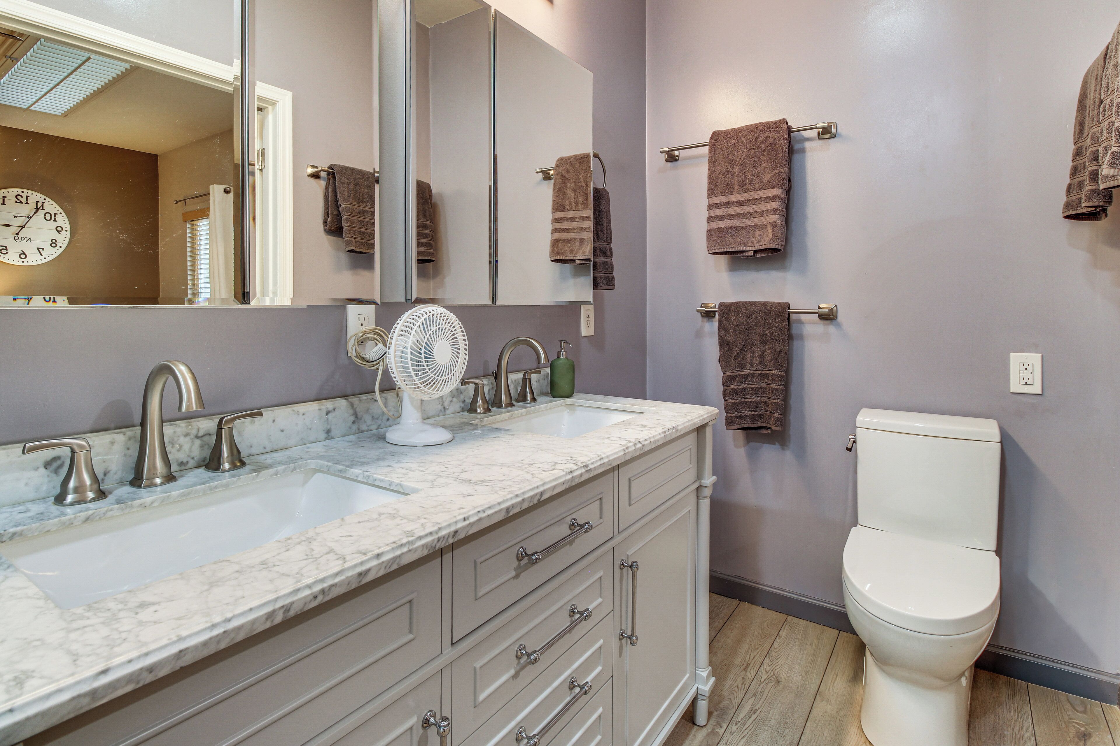 Une salle de bain avec deux lavabos, un miroir, un ventilateur et des toilettes.