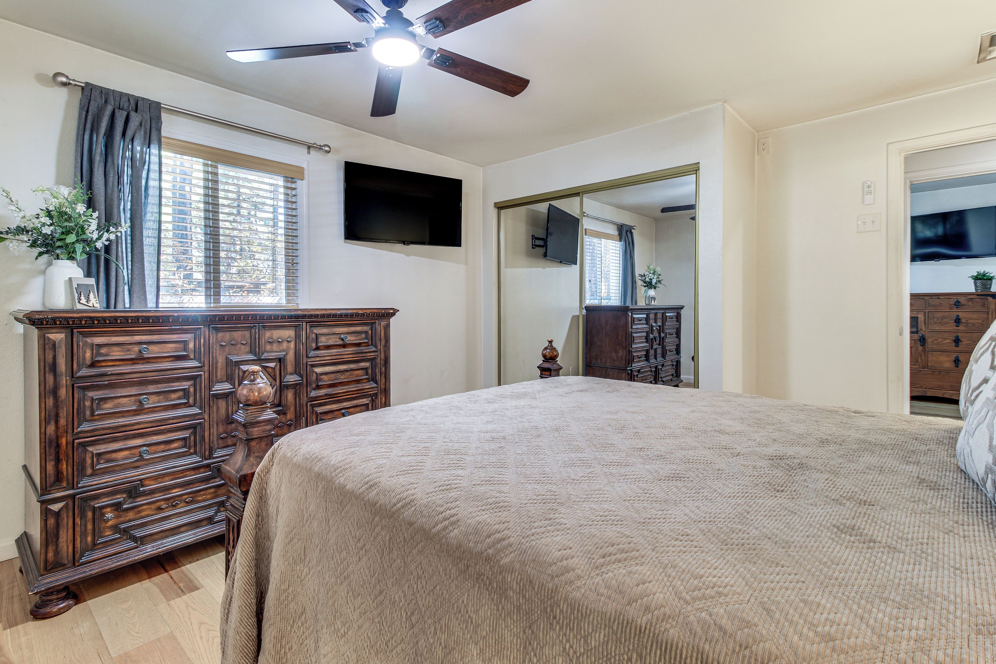 Une chambre à coucher comprenant un lit, une commode en bois, un ventilateur de plafond et un téléviseur à écran plat fixé au mur.