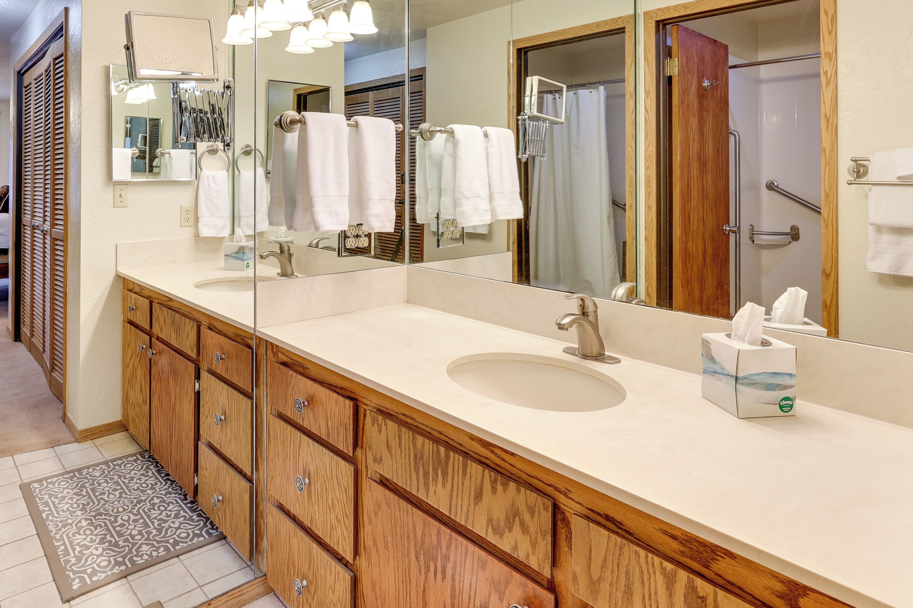 A bathroom with a large mirror, two sinks, wooden cabinets, and a towel rack.