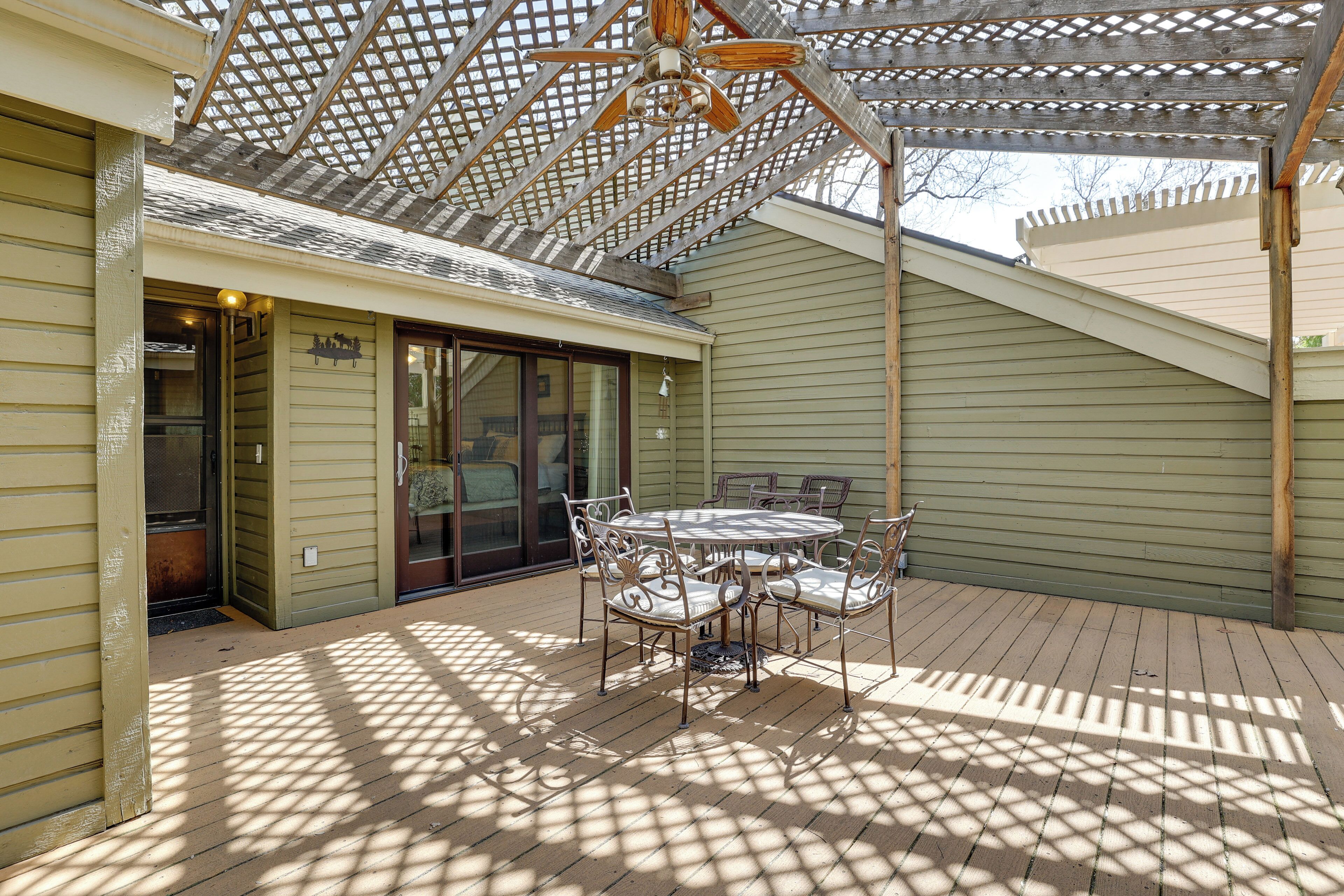 A covered patio with a table and chairs, a ceiling fan, and a pergola structure.