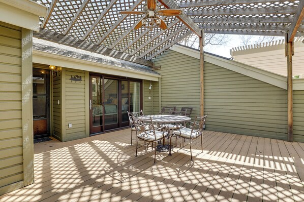 A covered patio with a table and chairs, a ceiling fan, and a pergola structure.