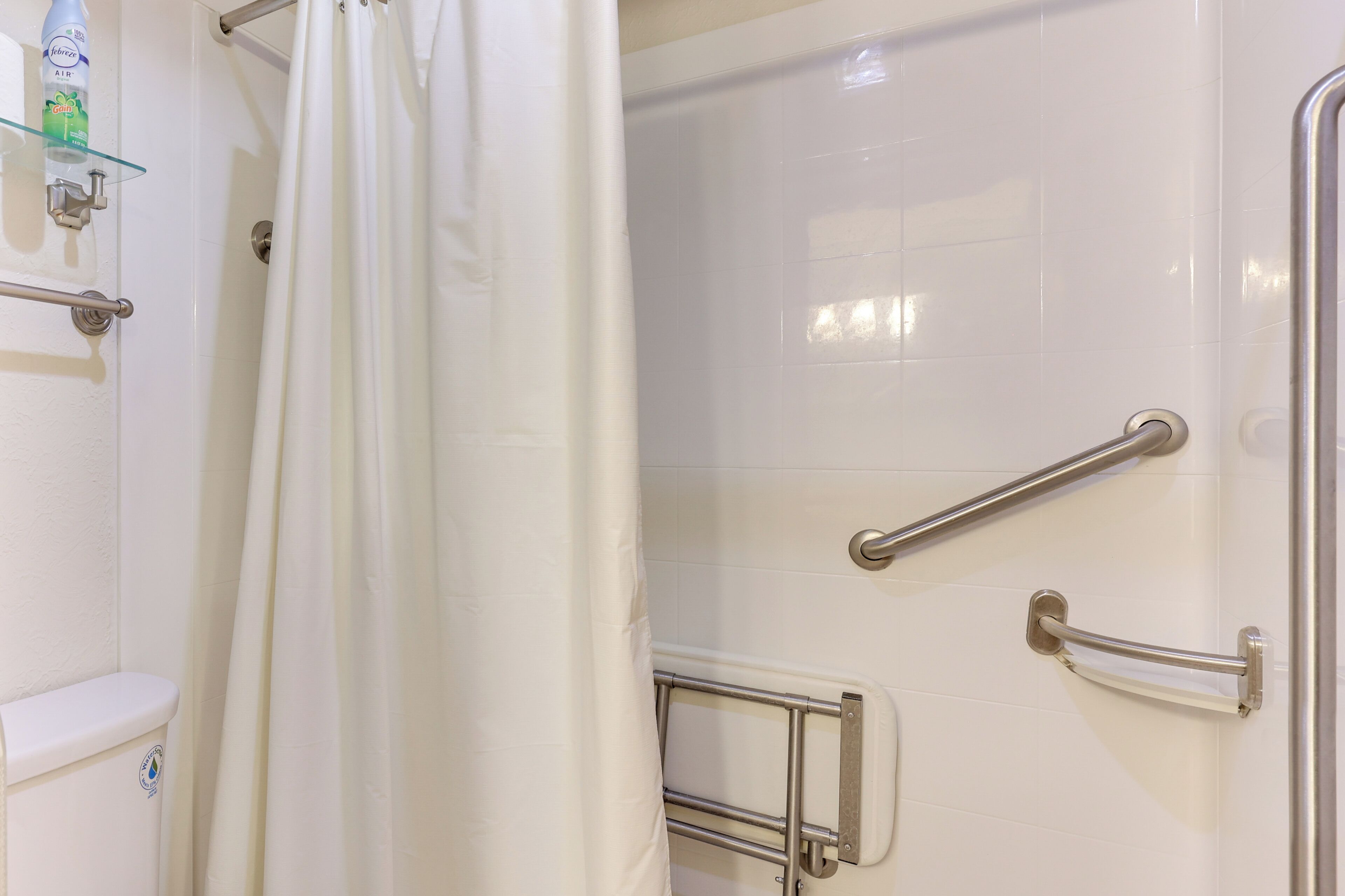 A bathroom with white tiles, a glass shelf with toiletries, and a shower curtain.
