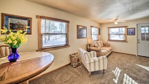 A living room with a wooden dining table, a sofa, and a chair. There are windows with blinds, a ceiling fan, and a door. - Sunroom, Deck & Grills: Marquette Cottage! (Marquette)