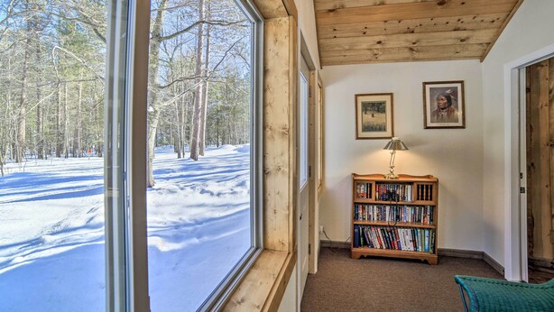 A room with a large window overlooking a snowy landscape, a bookshelf, and two framed pictures on the wall. - Sunroom, Deck & Grills: Marquette Cottage! (Marquette)