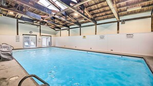 Une piscine intérieure dotée d’un haut plafond, de poutres apparentes et d’une horloge au mur.