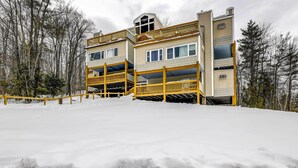 Un immeuble à plusieurs étages doté de balcons en bois, entouré de neige et d’arbres.