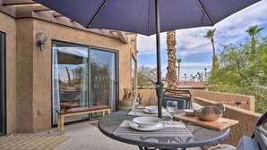An outdoor patio with a round table set for dining, a bench, and a large umbrella providing shade.