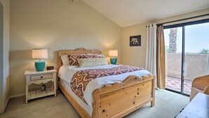 A bedroom with a wooden bed, two bedside tables with lamps, a nightstand with a drawer, and a view through a sliding glass door to an outdoor area.