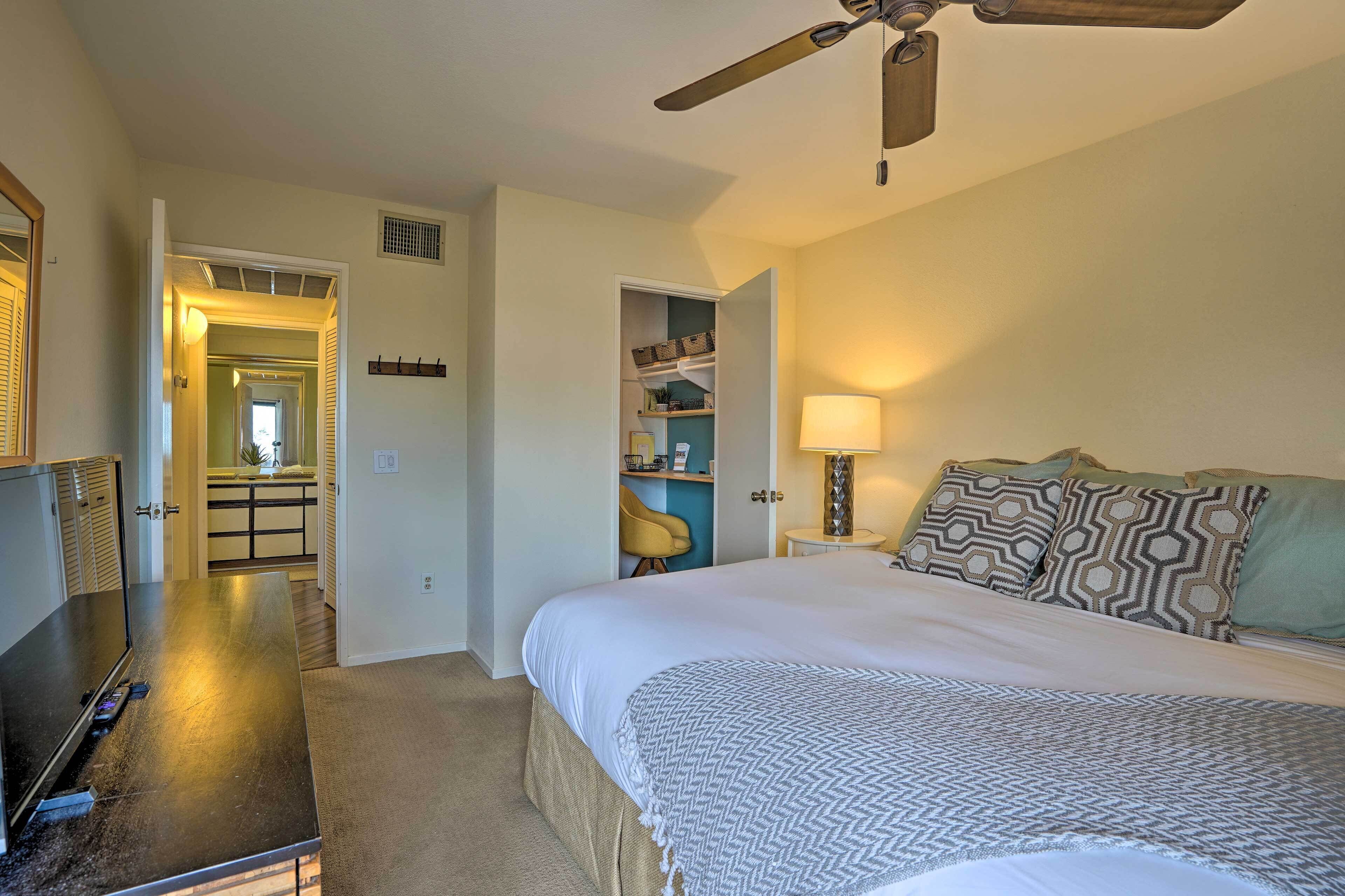 A hotel room with a bed, a ceiling fan, a desk, and a chair.