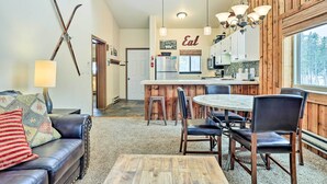 Ein gemütliches Wohnzimmer mit einer Ledersofa, einem Holztisch und einem Essbereich mit rundem Tisch und Stühlen. Im Hintergrund ist eine Küche mit Holzschränken und einem Kühlschrank zu sehen.