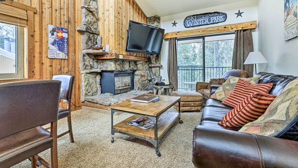Ein gemütliches Wohnzimmer mit Kamin aus Stein, einem an der Wand montierten Fernseher, einer Couch mit gemusterten Kissen und einem Schild mit der Aufschrift "SKI WINTER PARK".