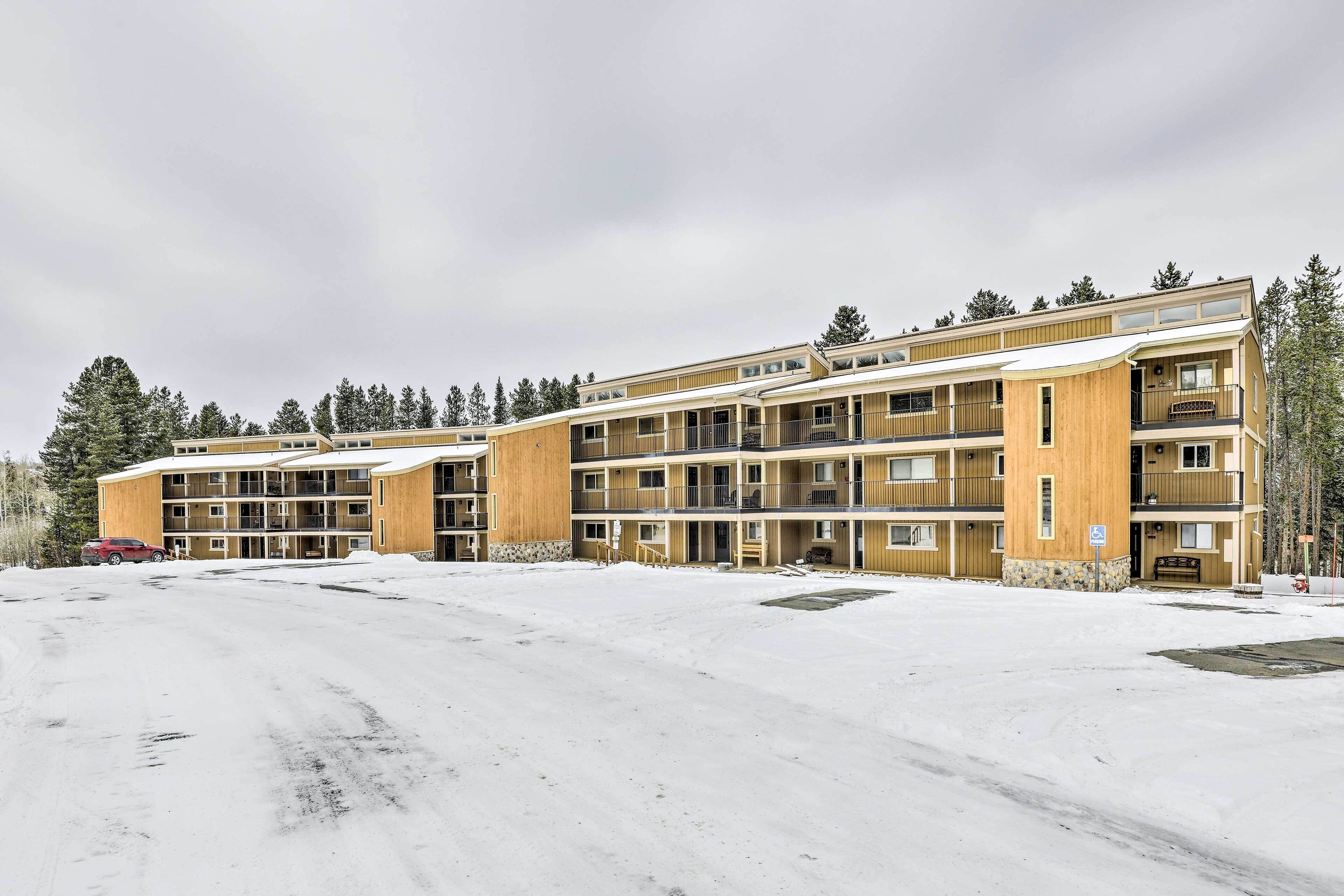 Un hotel de varios pisos con fachada de madera, varios balcones y un estacionamiento cubierto de nieve.