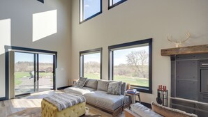 A spacious living room with a large sofa, a coffee table, and a fireplace. There are large windows providing a view of the outdoors. - Large Home w/ Land in Prairie Farm! (Prairie Farm)