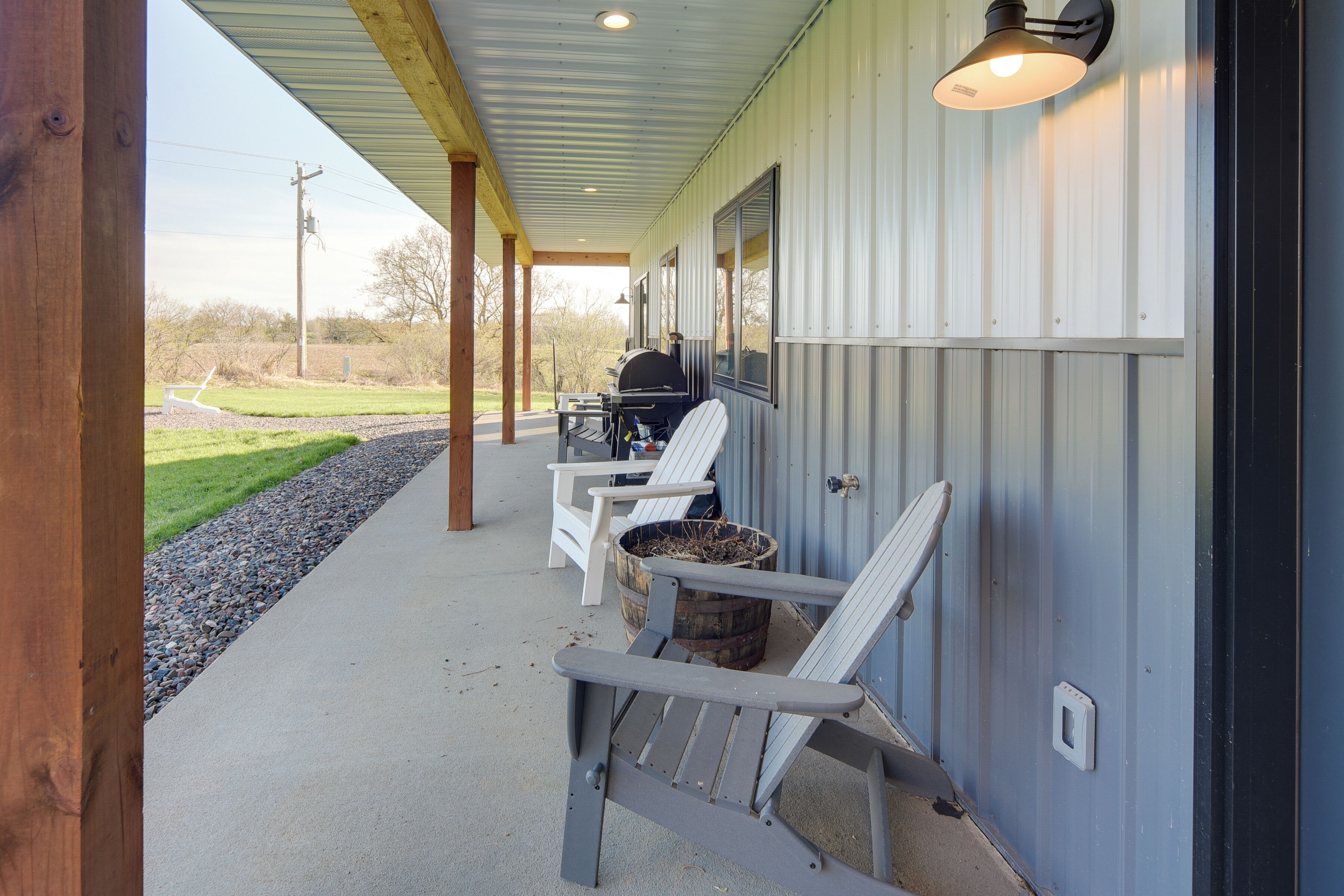 Une véranda couverte avec deux fauteuils Adirondack, un barbecue et un tonneau en bois.