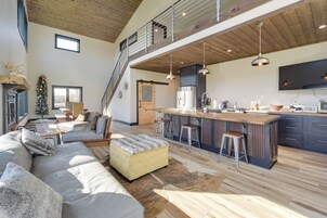 Ampla sala de estar com teto alto, um sofá grande, uma mesa de jantar de madeira e uma cozinha com eletrodomésticos modernos.