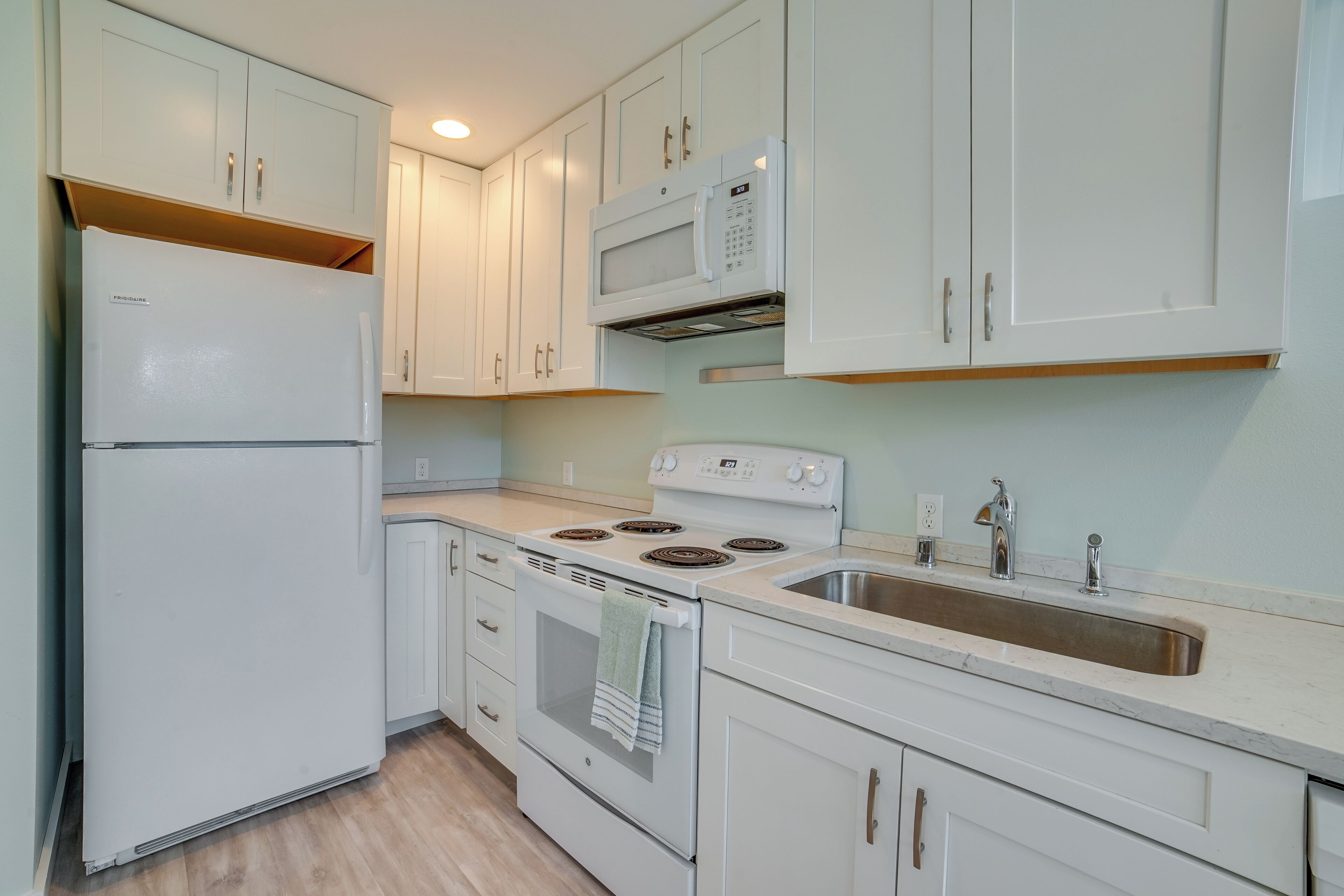 A kitchen with white cabinets, a refrigerator, a microwave, an oven, and a sink.