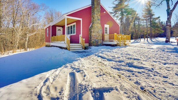 Une cabane rouge avec une cheminée en pierre, un porche en bois et une cour enneigée.