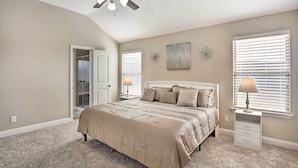 A bedroom with a bed, a ceiling fan, a nightstand, a lamp, and a window with blinds.