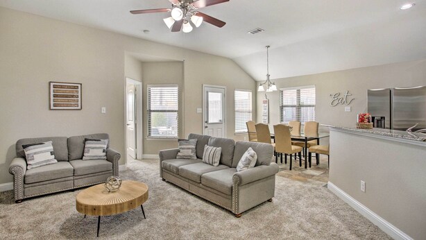 A spacious living room with a gray sofa, a coffee table, and a dining area with chairs and a chandelier.