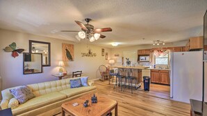 A living room with a sofa, coffee table, and a ceiling fan. There is a kitchen area with wooden cabinets and a refrigerator. - Pet-friendly Home w/ Grill & Farm in Meadowview! (Meadowview)