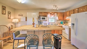 A kitchen with wooden cabinets, a central island with chairs, a refrigerator, and a microwave. - Pet-friendly Home w/ Grill & Farm in Meadowview! (Meadowview)
