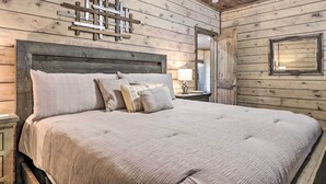 A wooden-paneled bedroom with a large bed, a wooden headboard, a wall-mounted mirror, and a bedside table with a lamp.