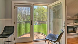 Une pièce dotée d’une porte-fenêtre coulissante donnant sur un balcon avec une rambarde en métal, une chaise noire et un four à micro-ondes posé sur une étagère.