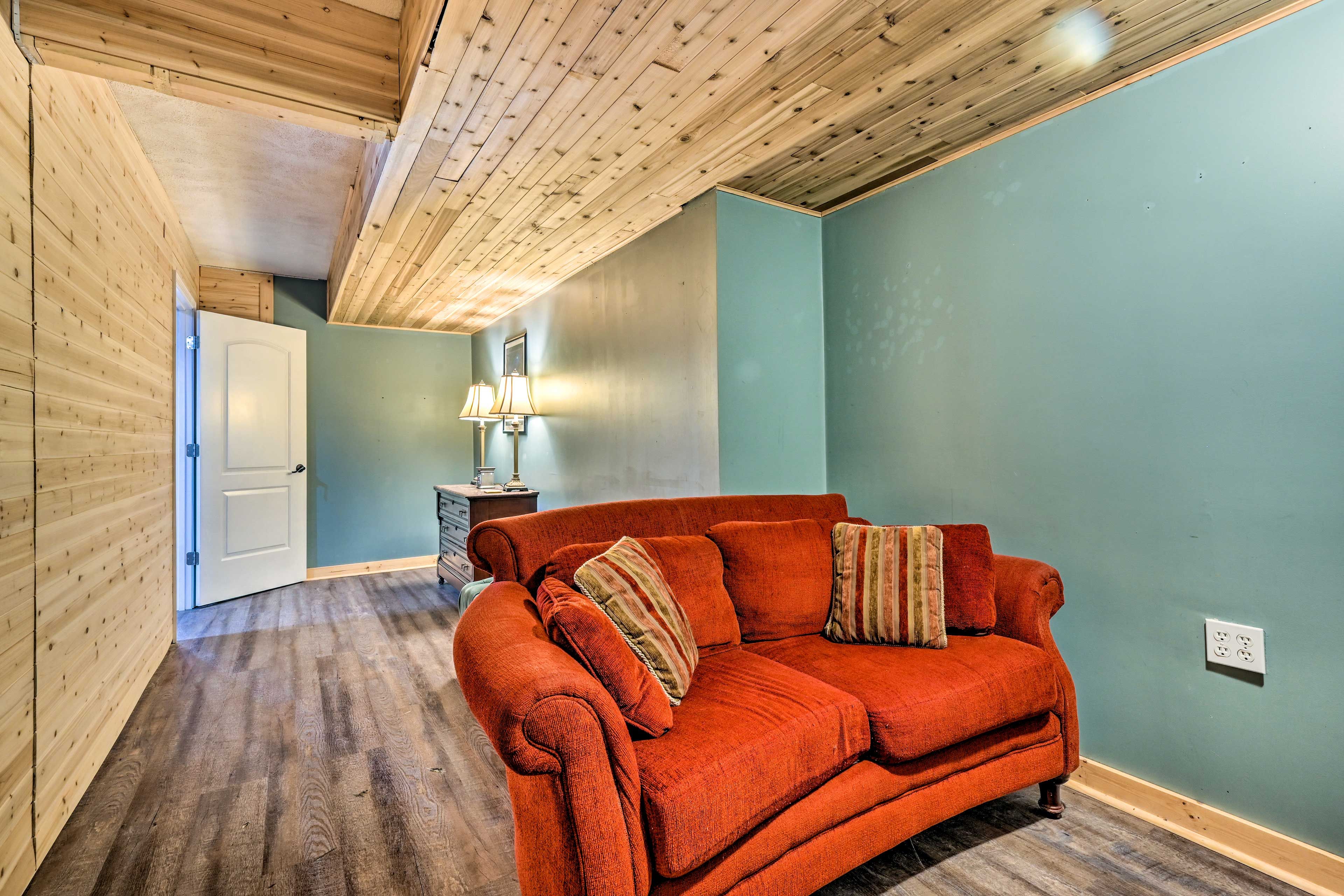 Ein Zimmer mit Holzbalkendecke, einem roten Sofa, einer Lampe und einer Tür.