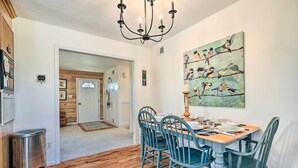 Un coin repas avec une table en bois et quatre chaises, un lustre et un tableau représentant des oiseaux accroché au mur.